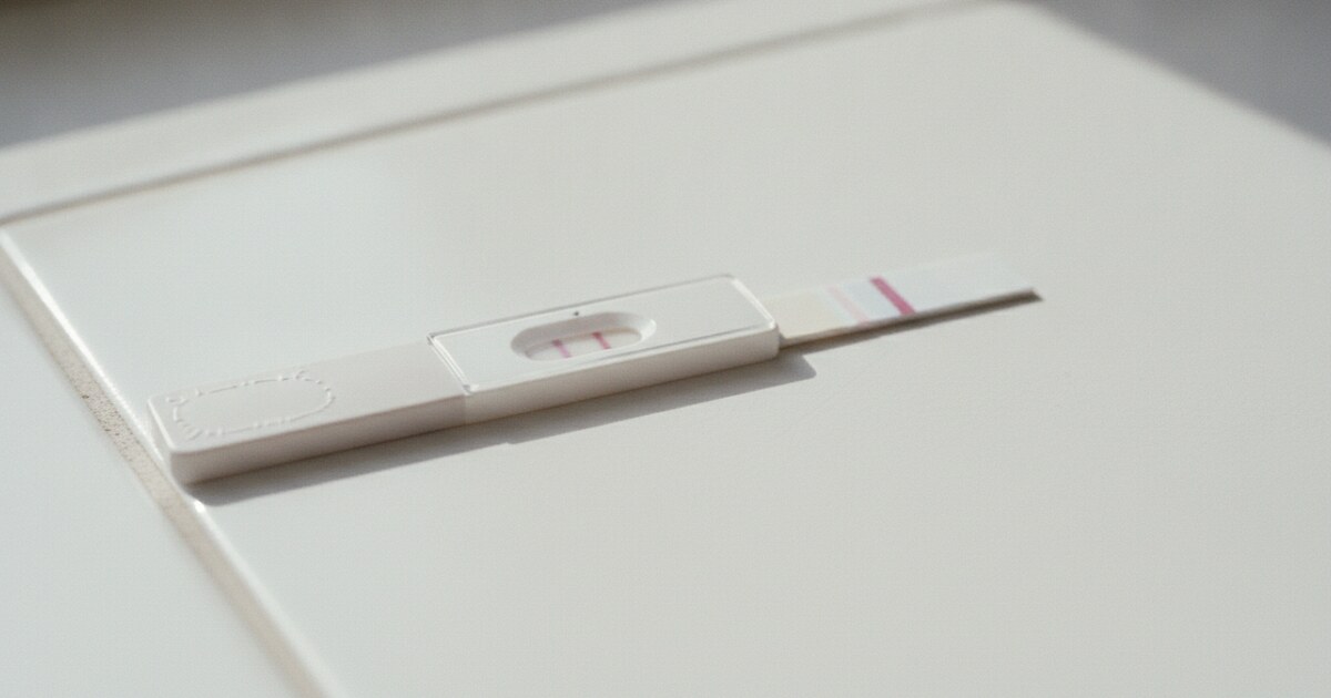 Home pregnancy test strip on a white surface in morning light, faint second line visible in the result window
