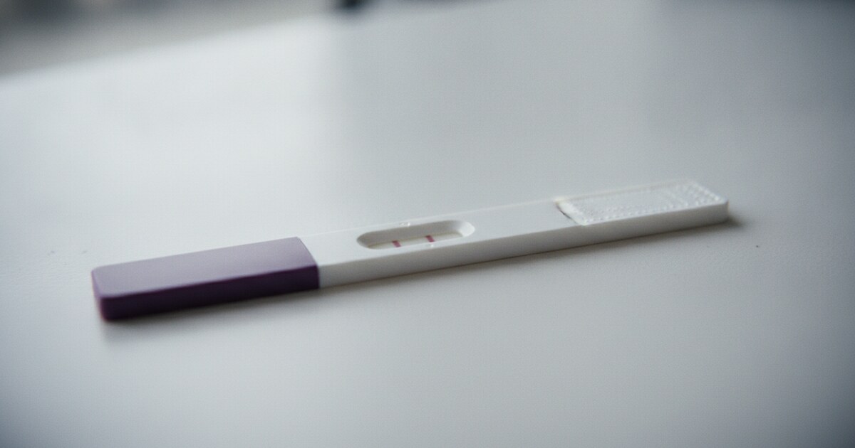 Home pregnancy test strip on a white surface showing a very faint second line, natural daylight