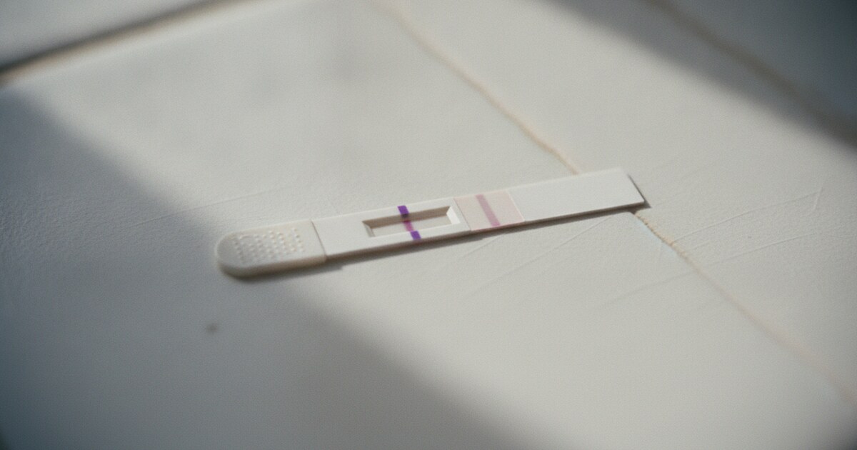 A strip ovulation test on a white surface showing a clearly bold control line and a noticeably lighter test line