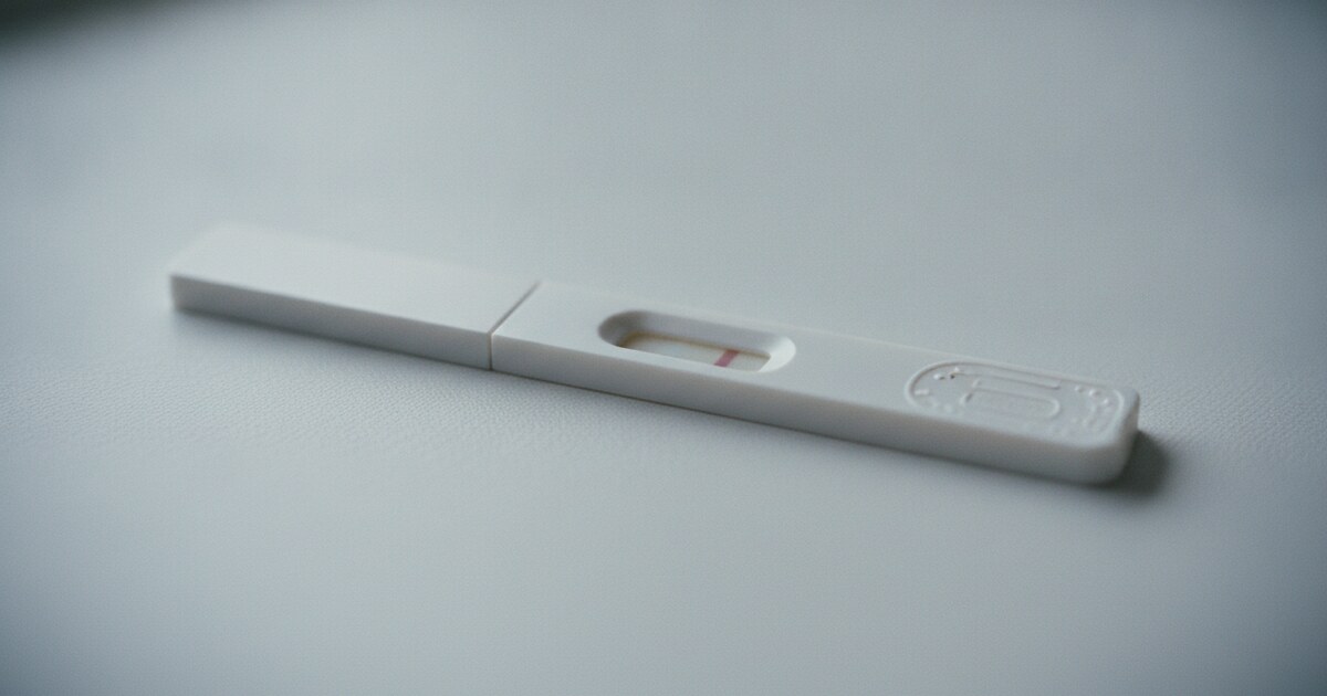 Close-up of a white pregnancy test strip on a clean white surface showing the faint colorless indent groove at the test line position